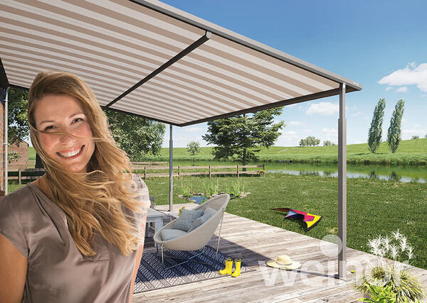 Frau auf Terrasse unter moderner Markise, Gartenmöbel und Natur im Hintergrund bei Sonnenschein.
